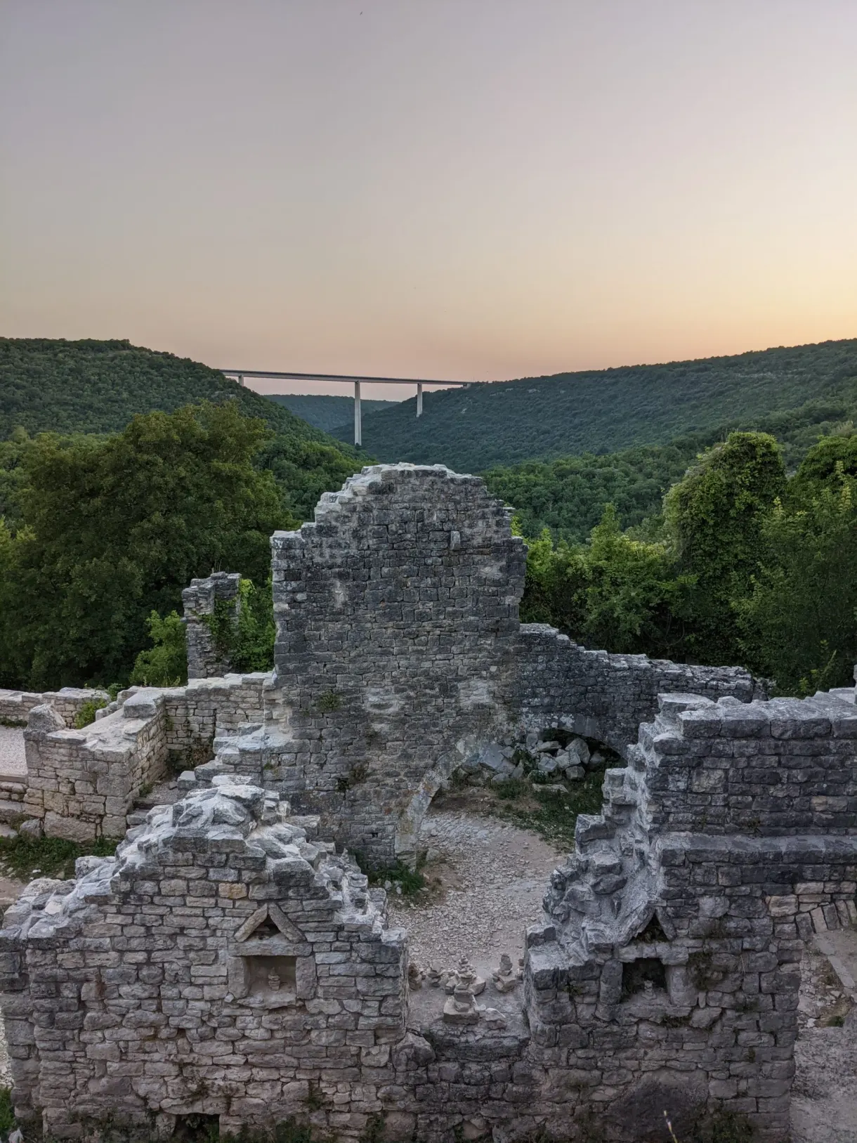 Collapsed church walls of Dvigrad at dusk, viaduct in the distance