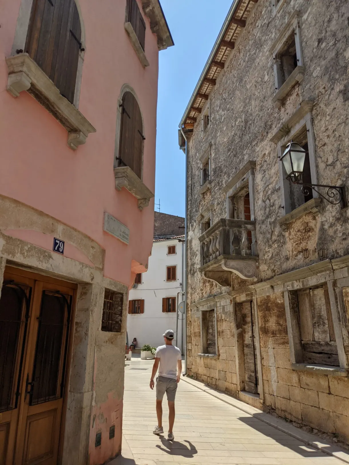Passer-by in a street of Vodnjan between a pink façade and a stone wall