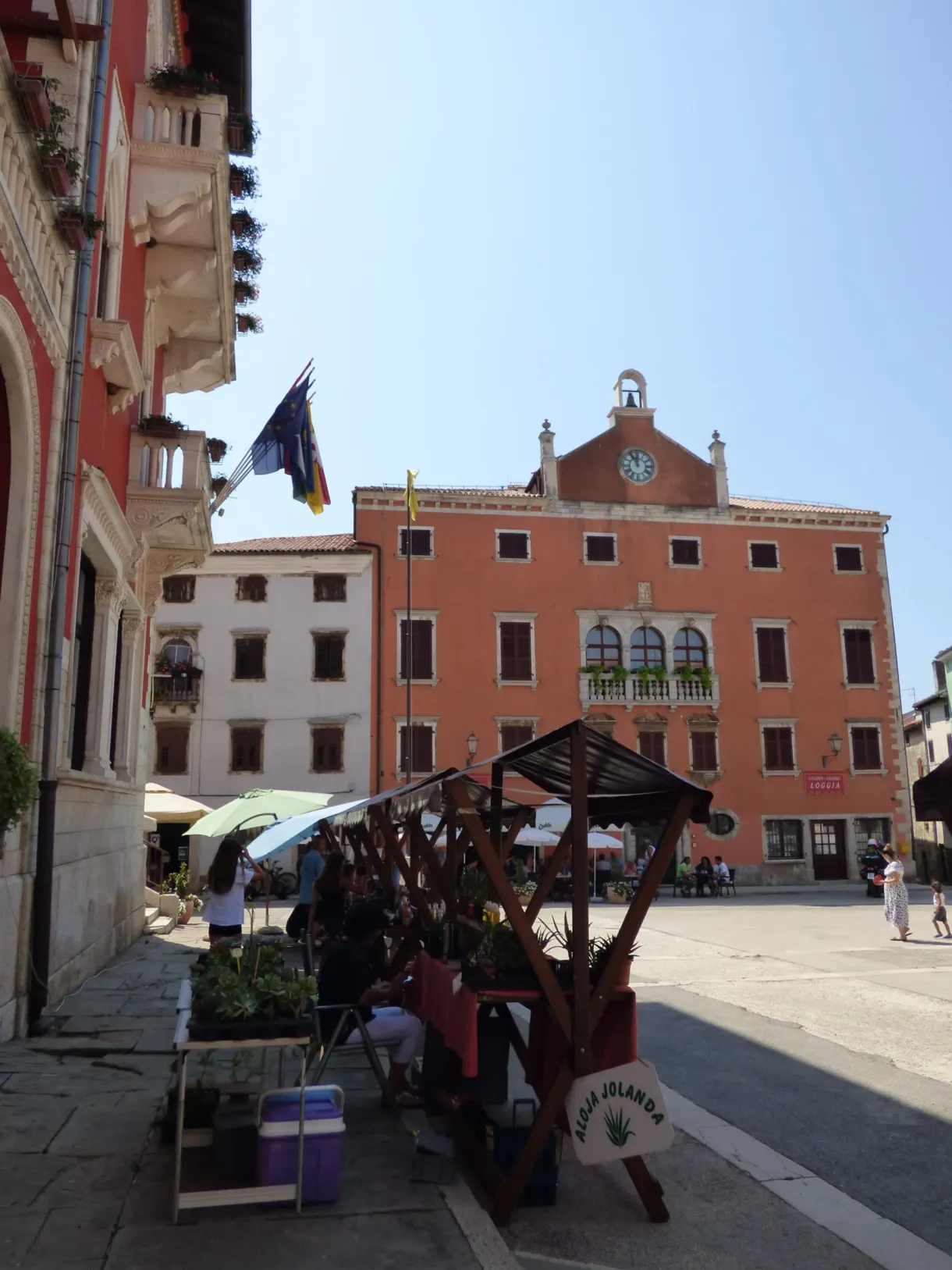 Market stall under an awning in front of the red palace of Vodnjan