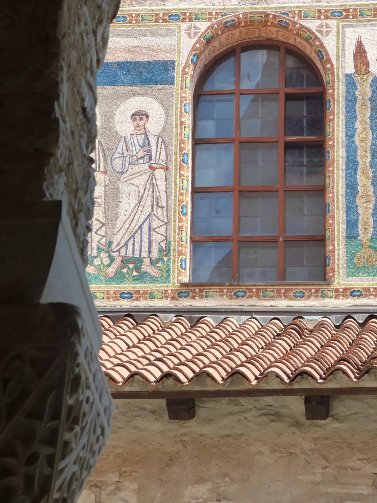Mosaic of a saint around a window on the façade, above the roof tiles
