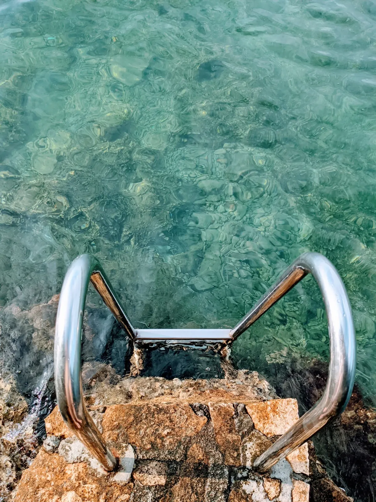 Stainless steel bathing ladder set into a rock, turquoise water