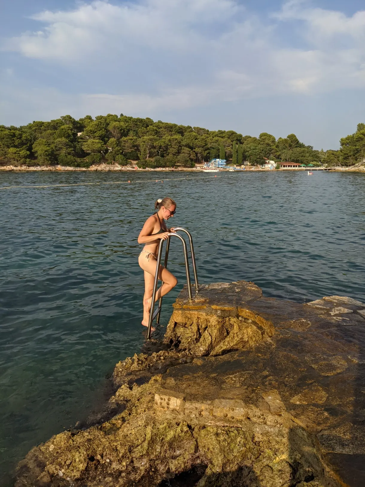 Woman going into the water down the ladder of a rocky cove