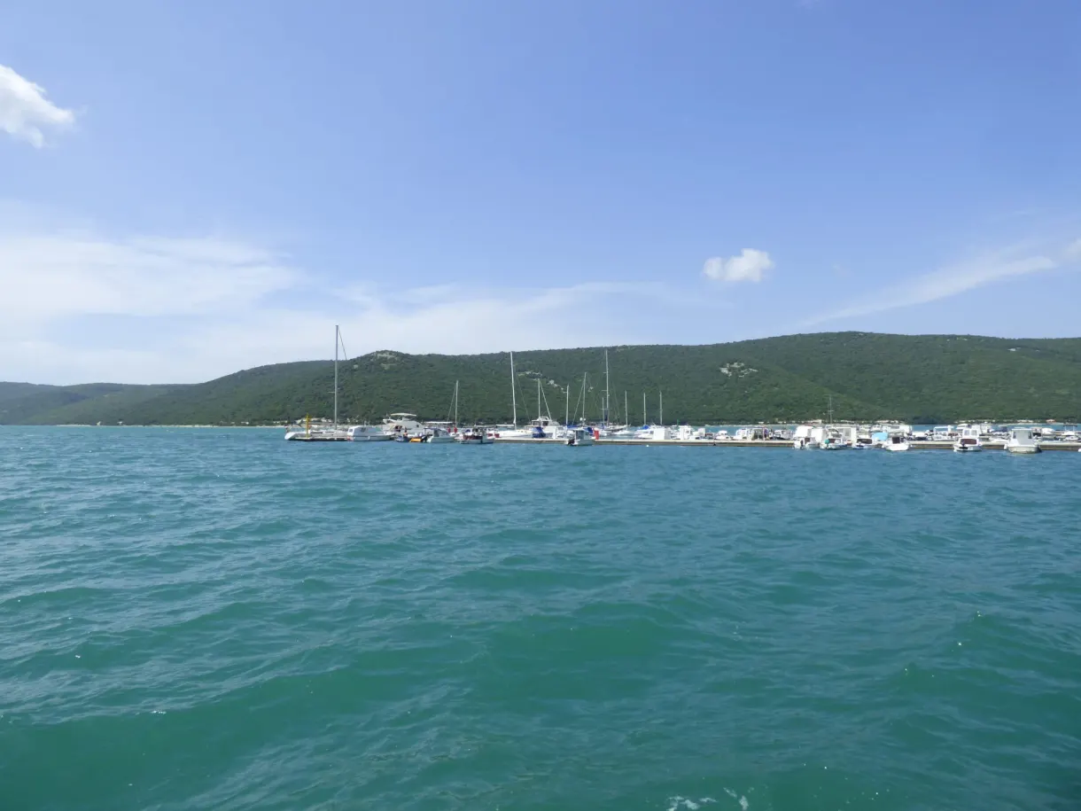 Masts of sailing boats and turquoise water in front of the hills of Trget