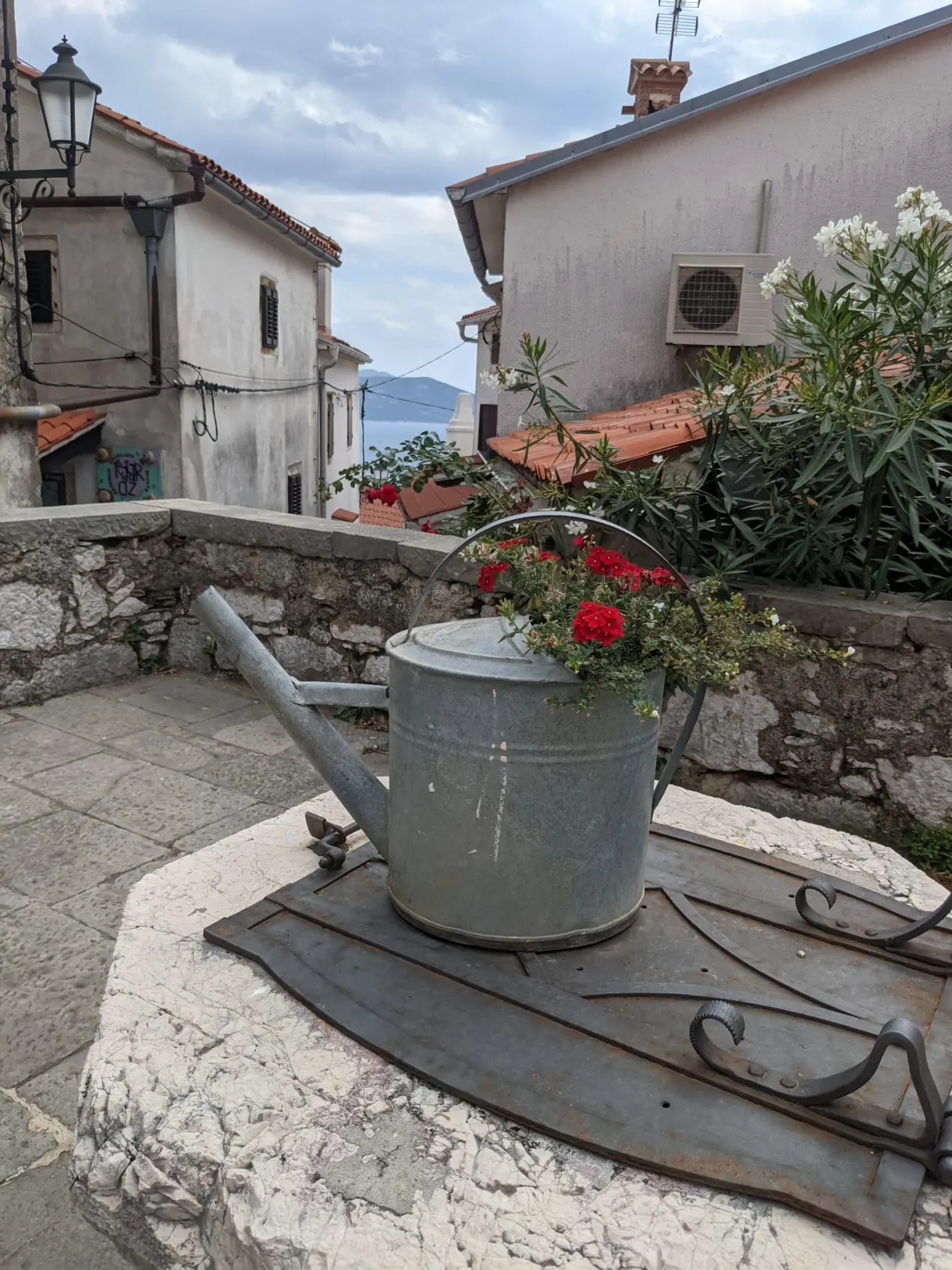 Zinc watering can filled with flowers on a low wall in the village of Brseč
