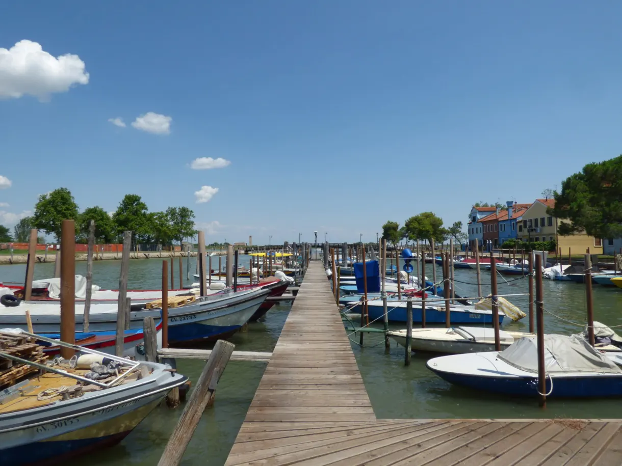 Ponton de bois entre barques amarrées face aux maisons colorées