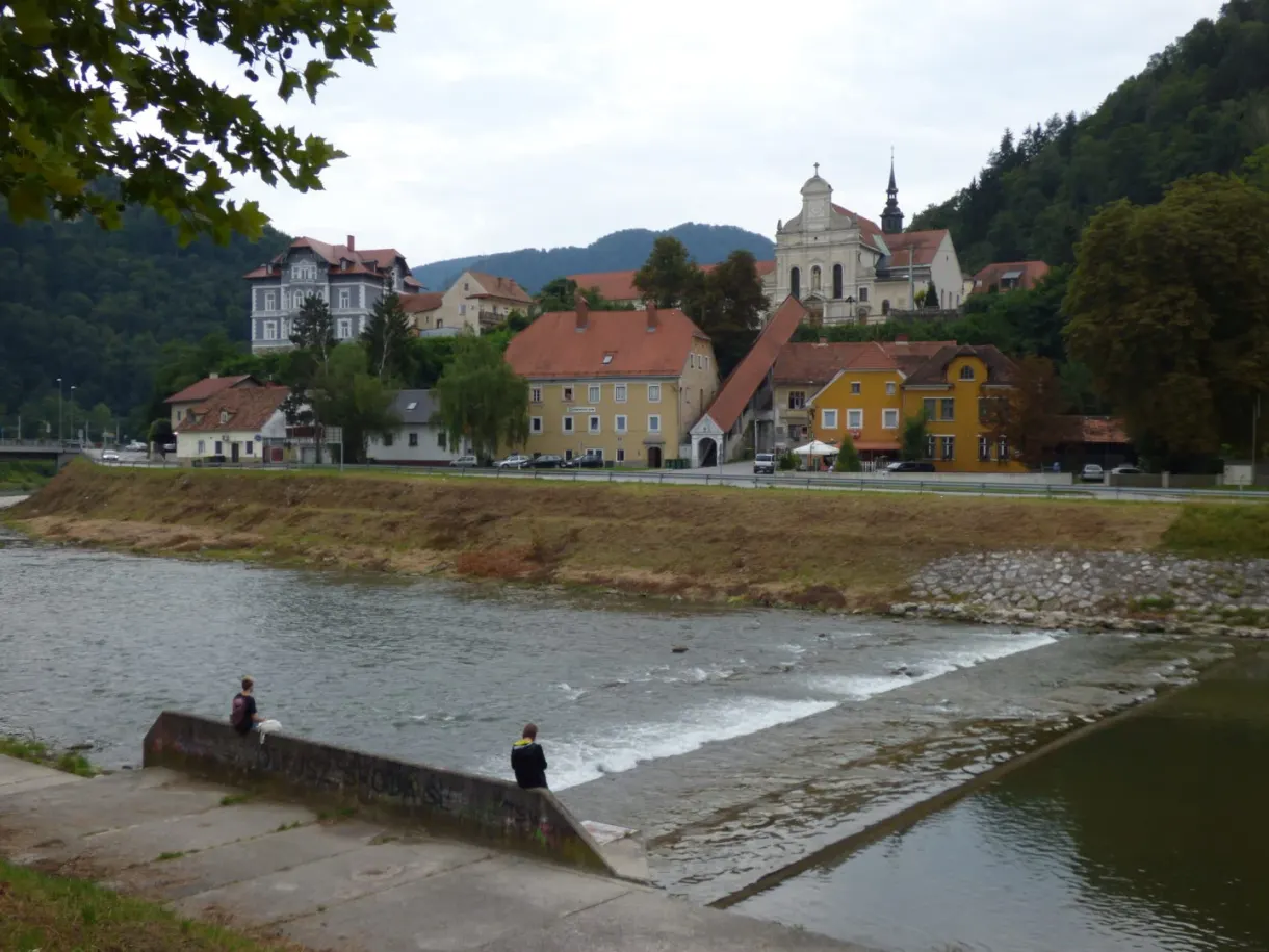 River flowing over a weir in front of colourful houses and a wooded hill