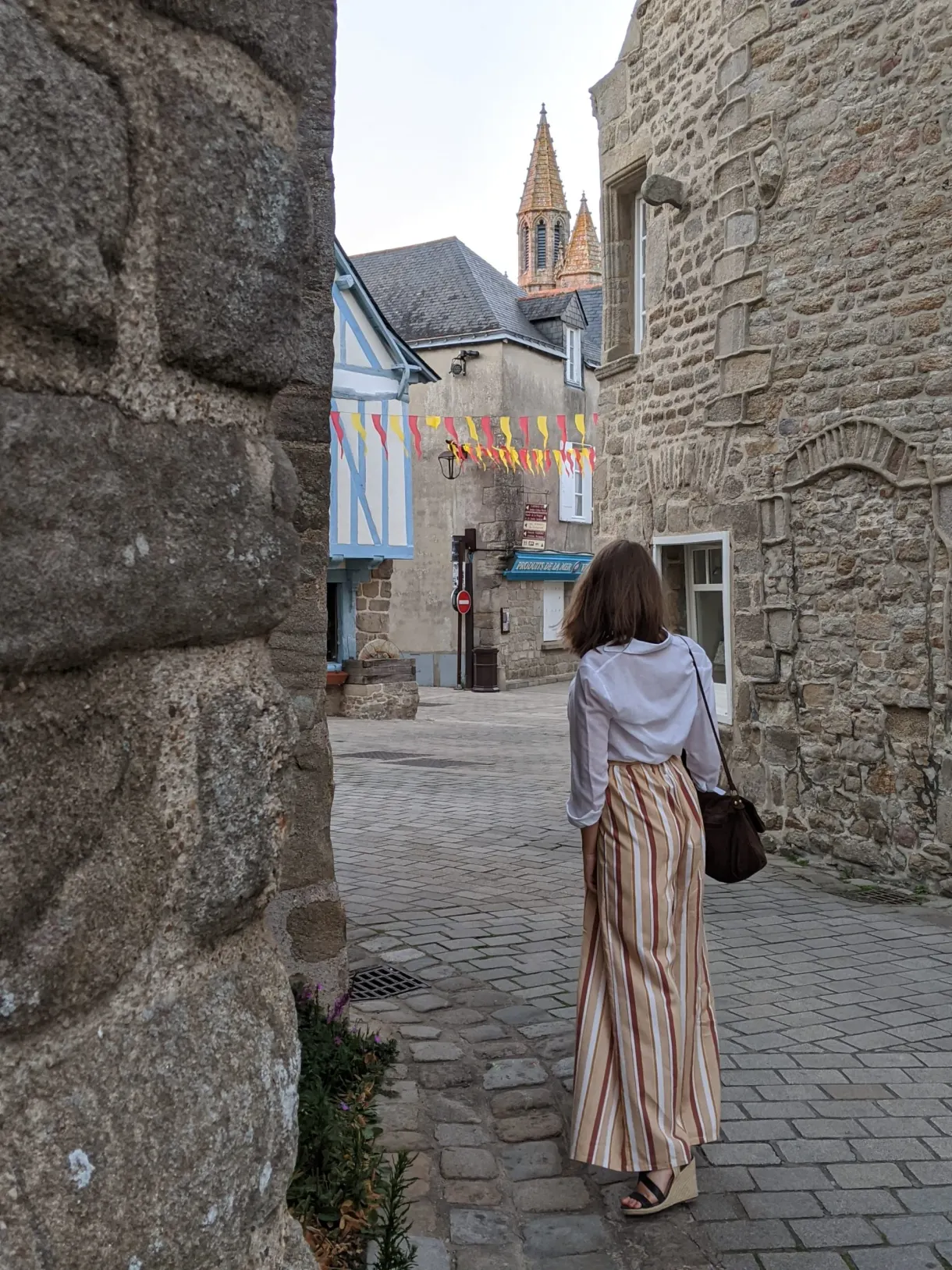 Woman seen from behind walking up a cobbled lane towards the bell tower