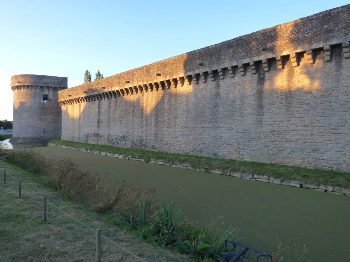 Round tower and crenellated curtain wall reflected in the moat