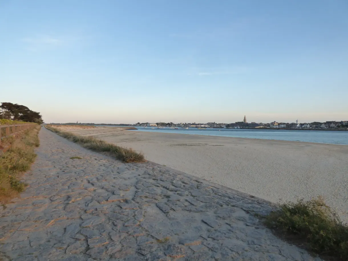 Paved path running along a vast pale sandy beach