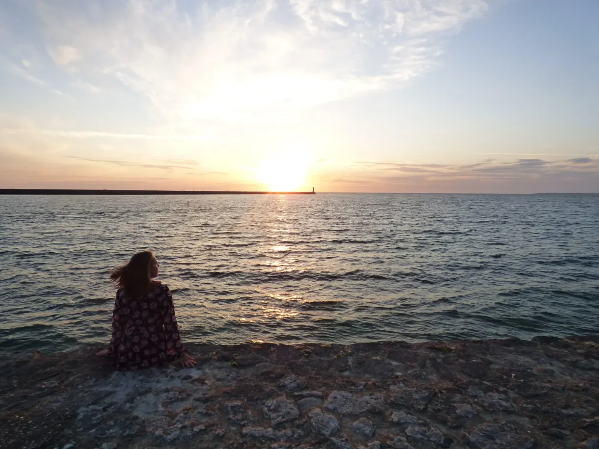 Woman sitting on the rocks facing the setting sun