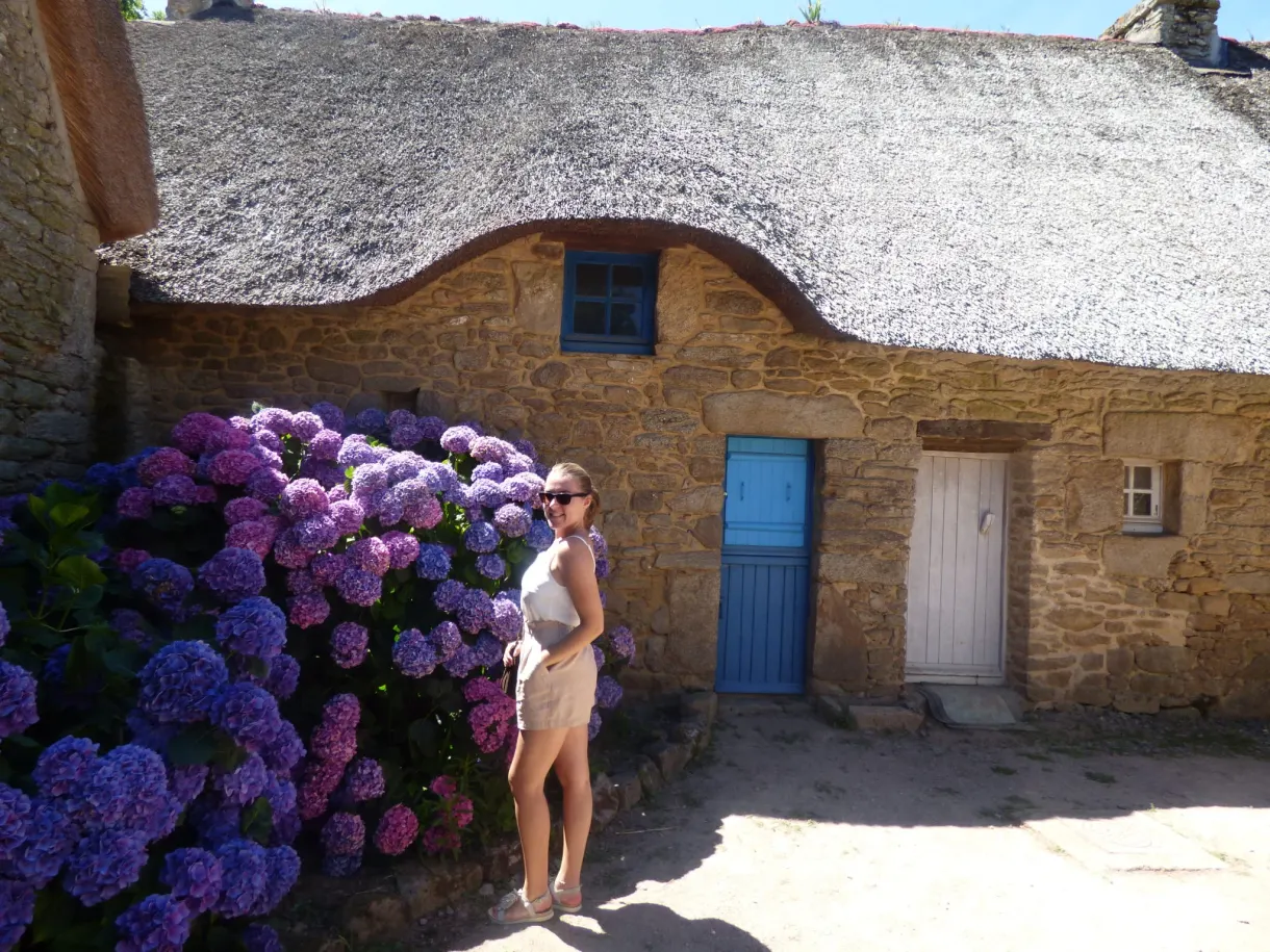 Woman posing in front of a cottage and its purple hydrangeas