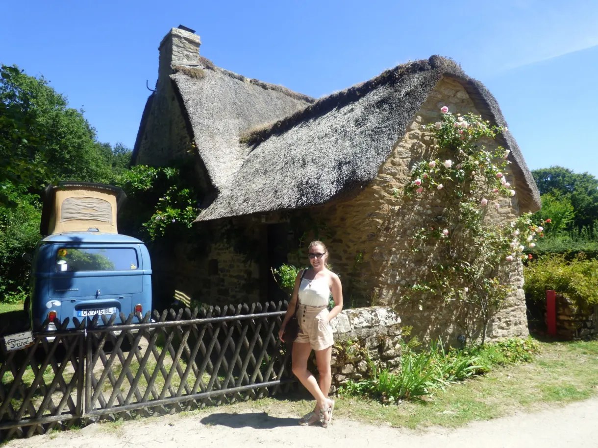 Old blue van parked in front of a flower-decked cottage