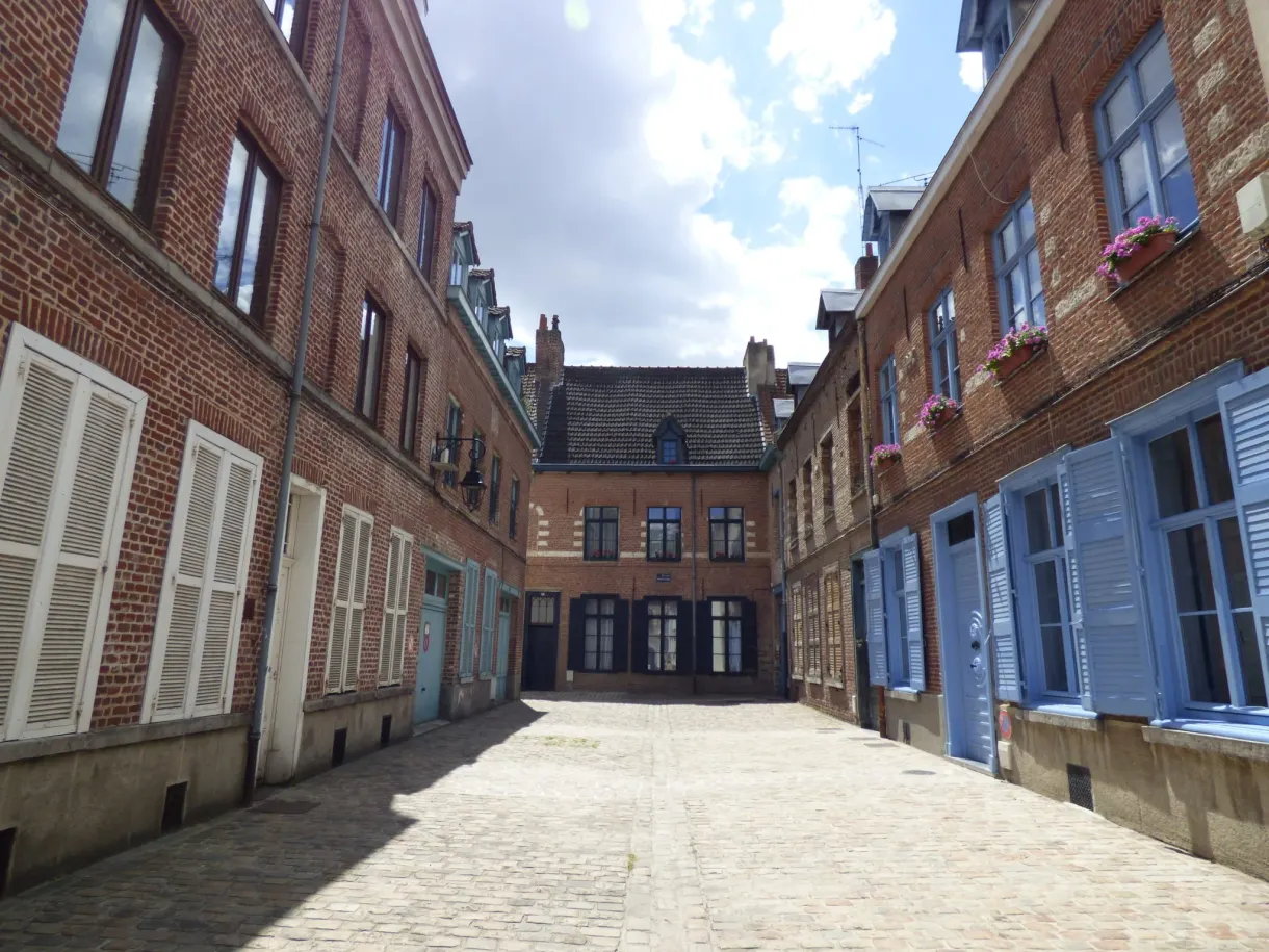 Cour pavée entourée de maisons de brique aux volets bleus