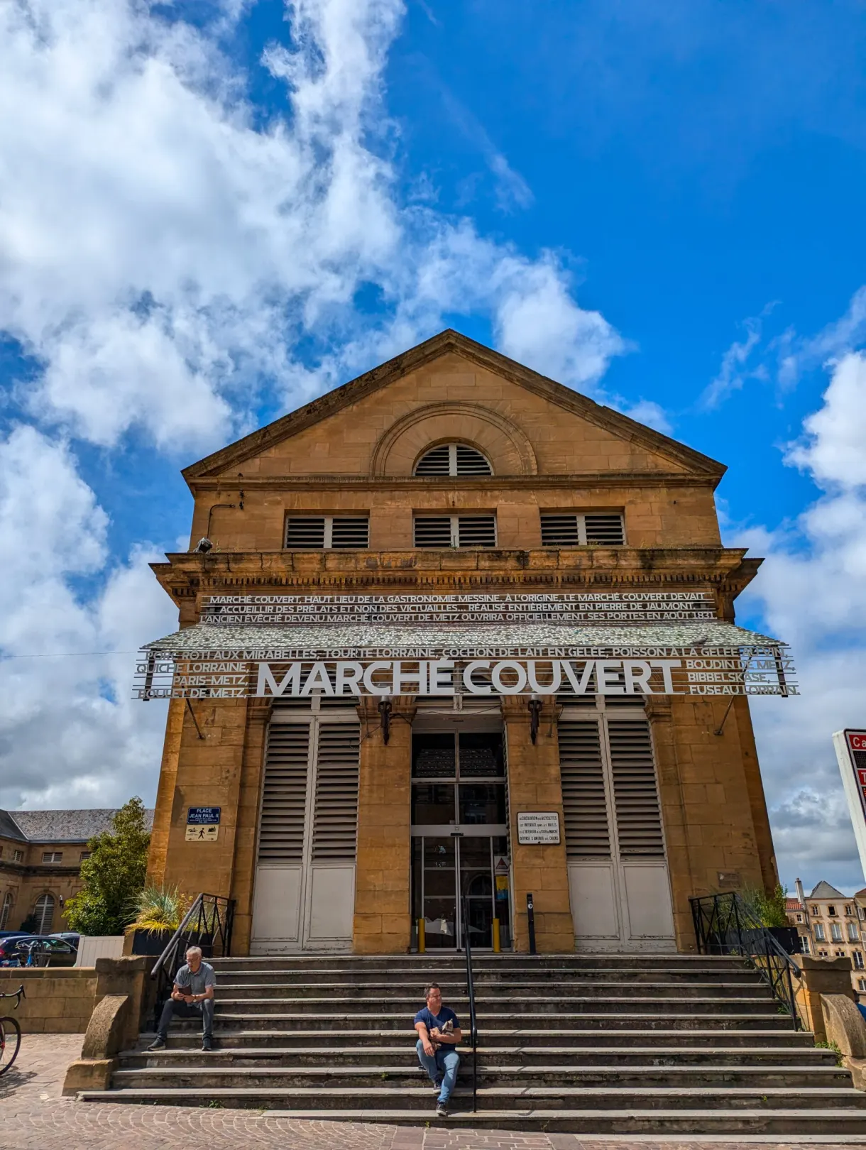 Fronton en pierre du marché couvert de Metz, promeneurs assis sur les marches
