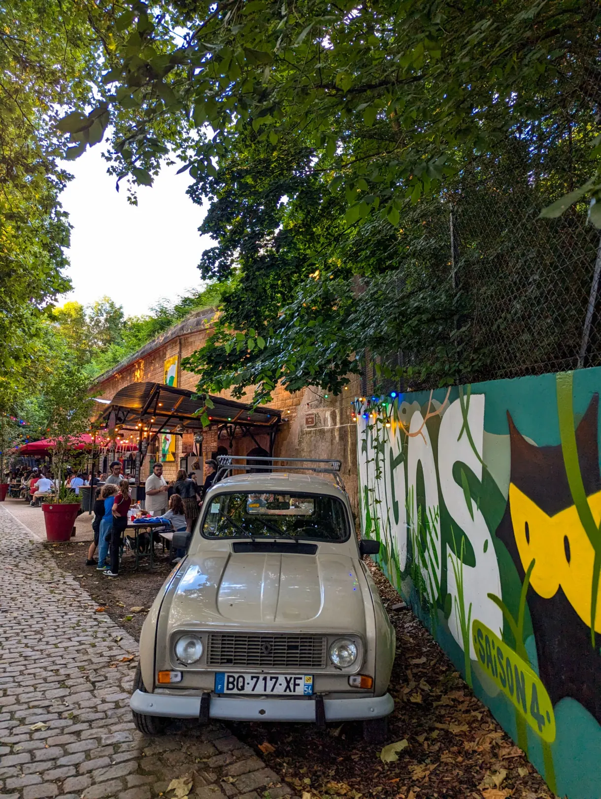 Vieille Renault 4 beige garée devant une guinguette et une fresque colorée