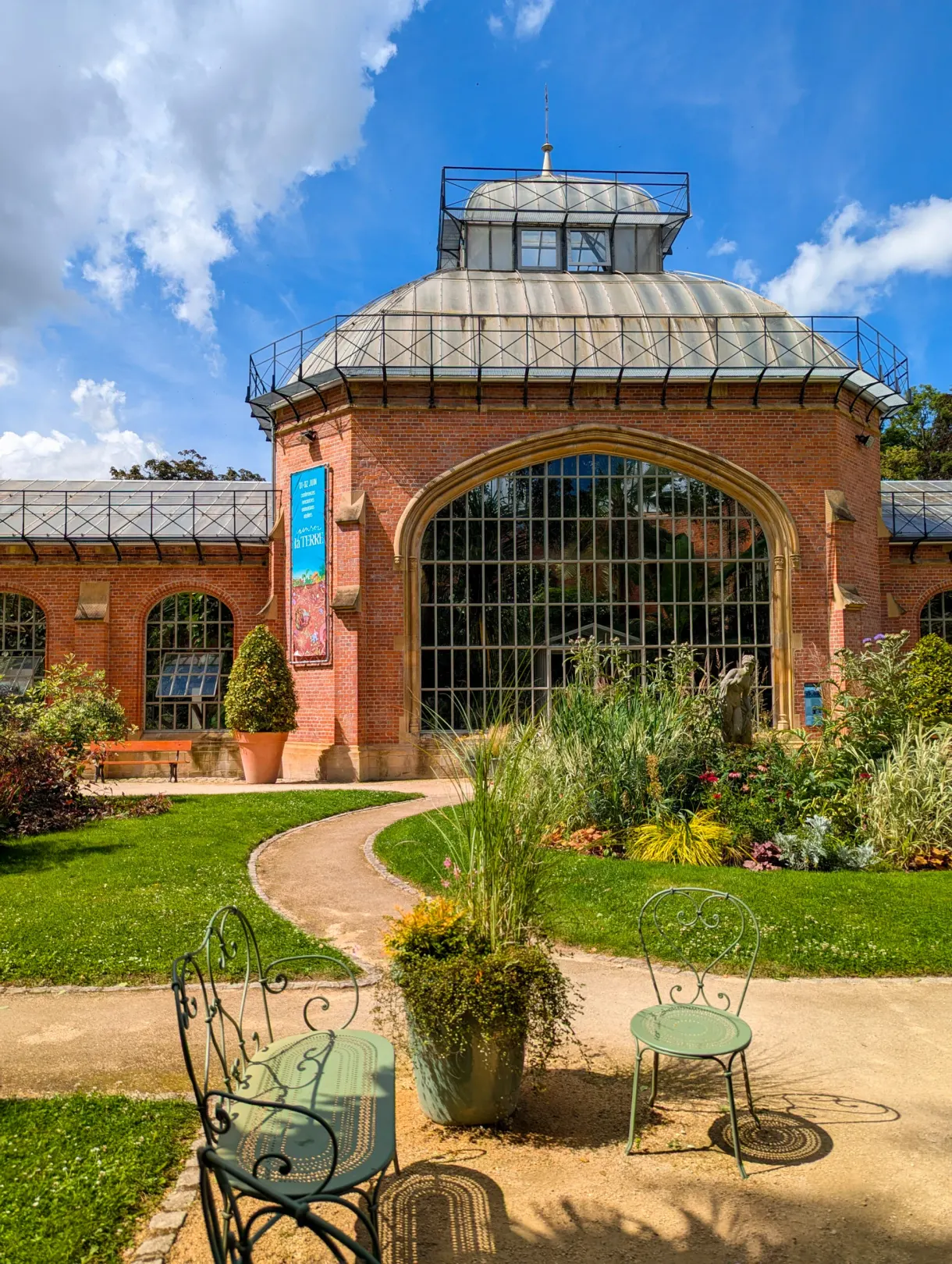 Grande serre en brique du jardin botanique et chaises en fer vert