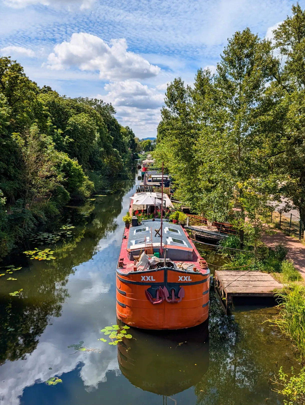 Péniche rouge amarrée sur un canal bordé d'arbres, vue en plongée