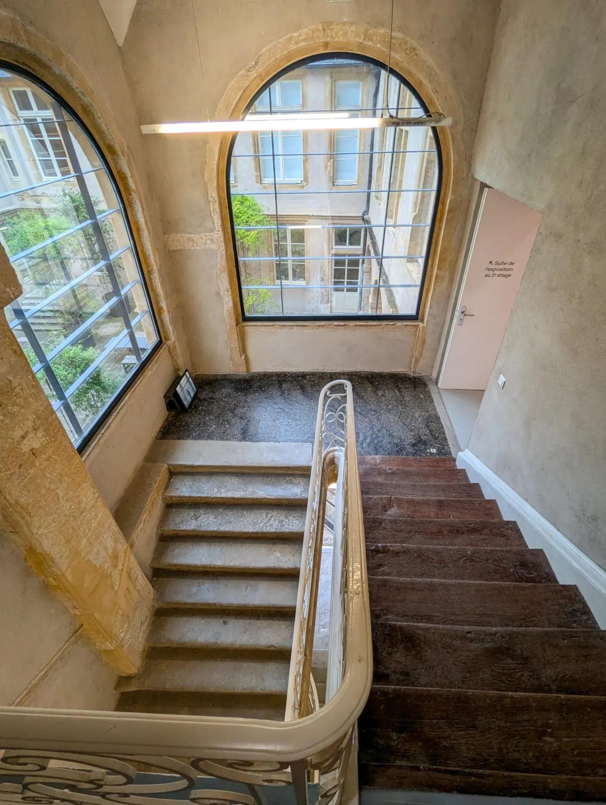 Escalier ancien en pierre claire sous de hautes fenêtres cintrées