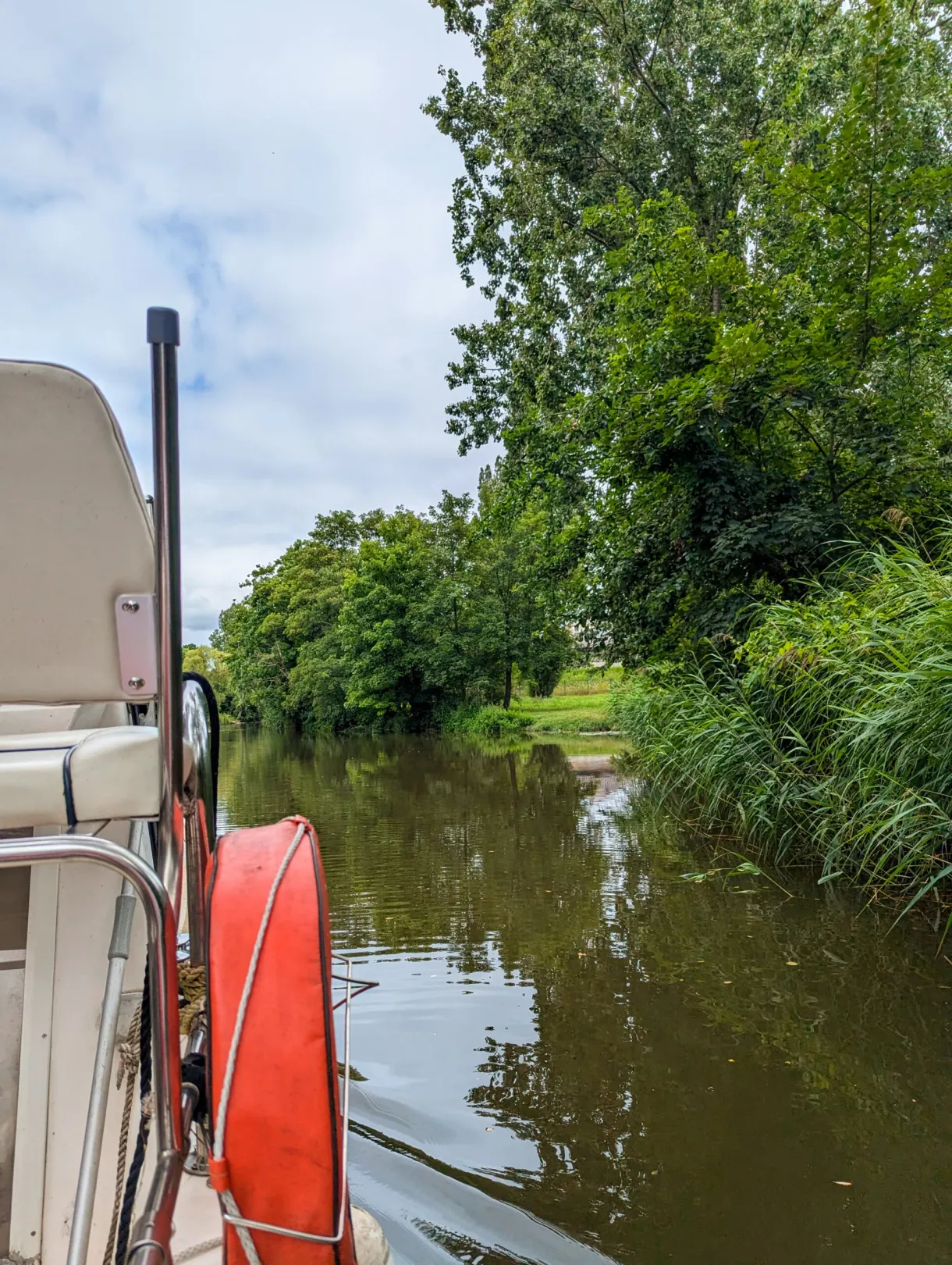 Proue du bateau et bouée orange sur un bras d'eau bordé de roseaux