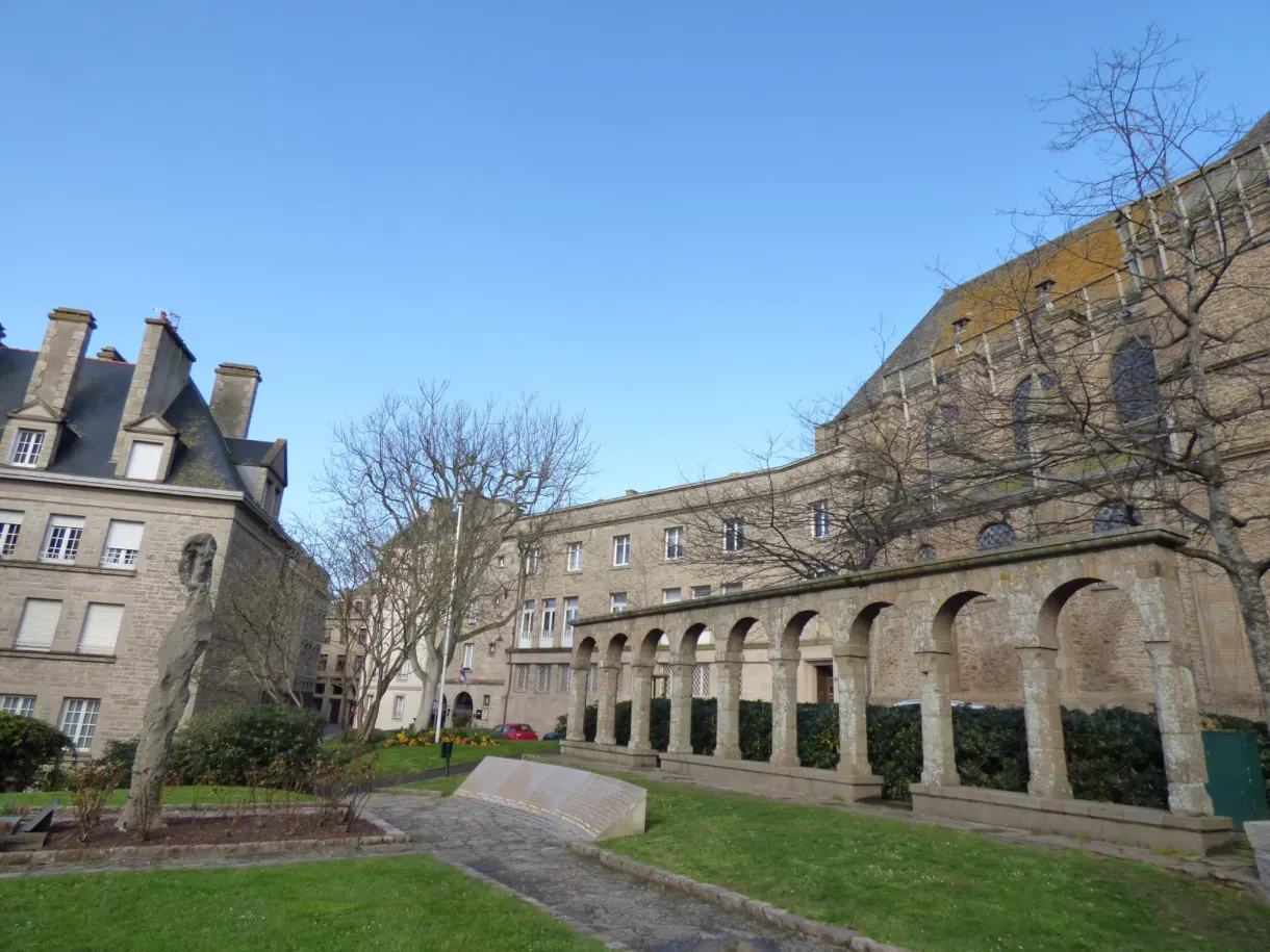 Longue galerie d'arcades bordant une pelouse au pied des remparts