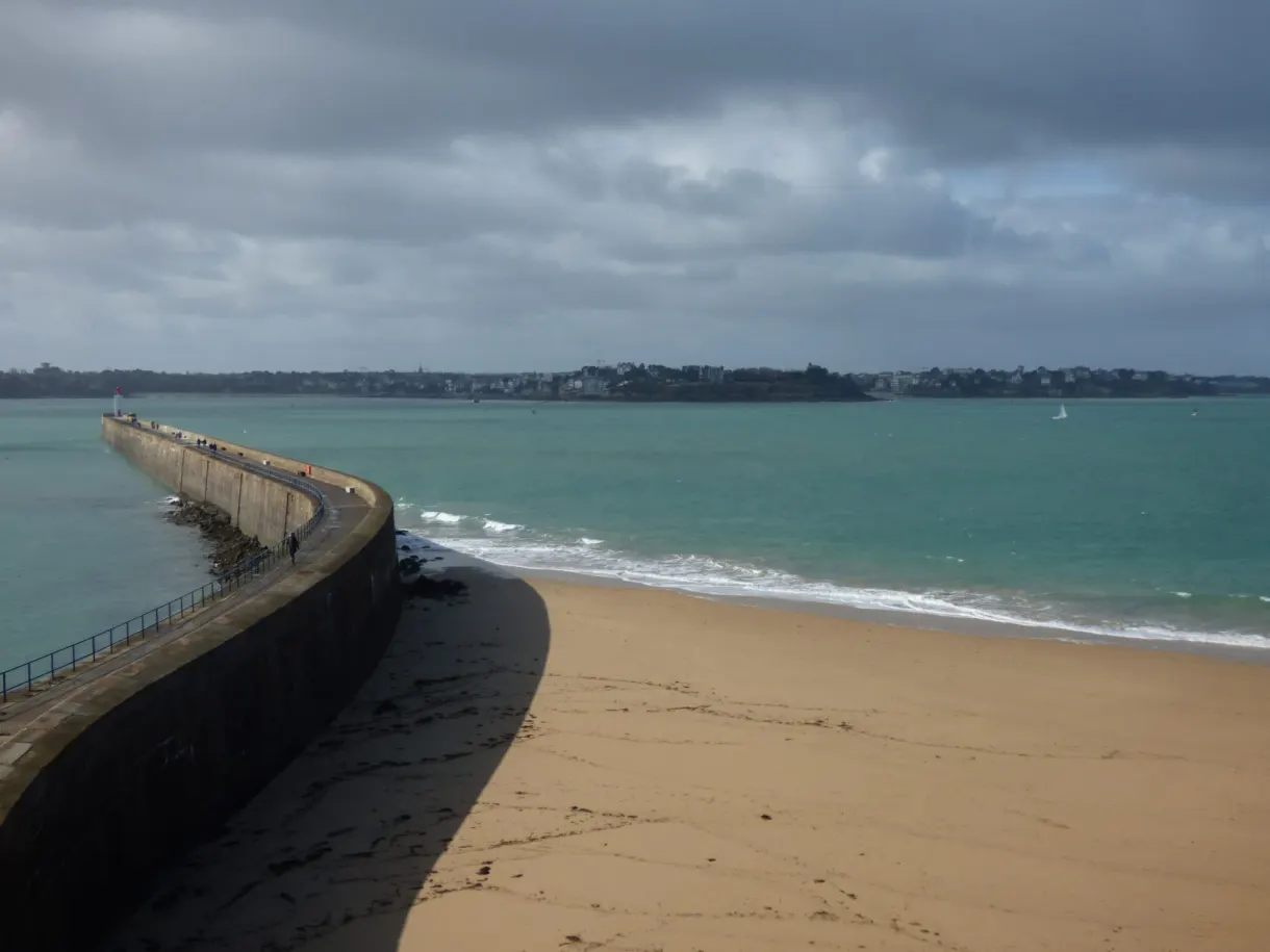 Longue digue et plage de sable sous un ciel chargé