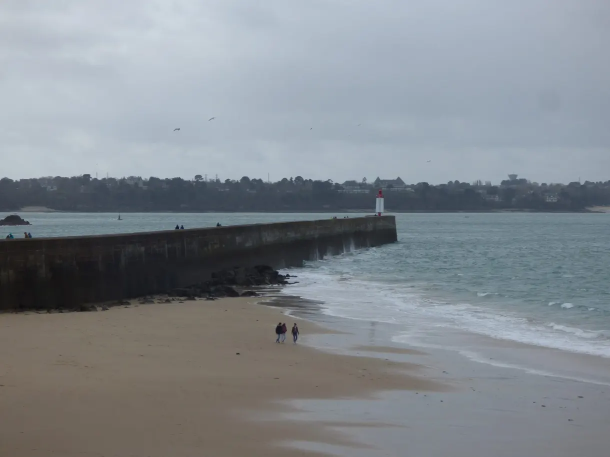 Môle de pierre et balise rouge au bord d'une plage grise