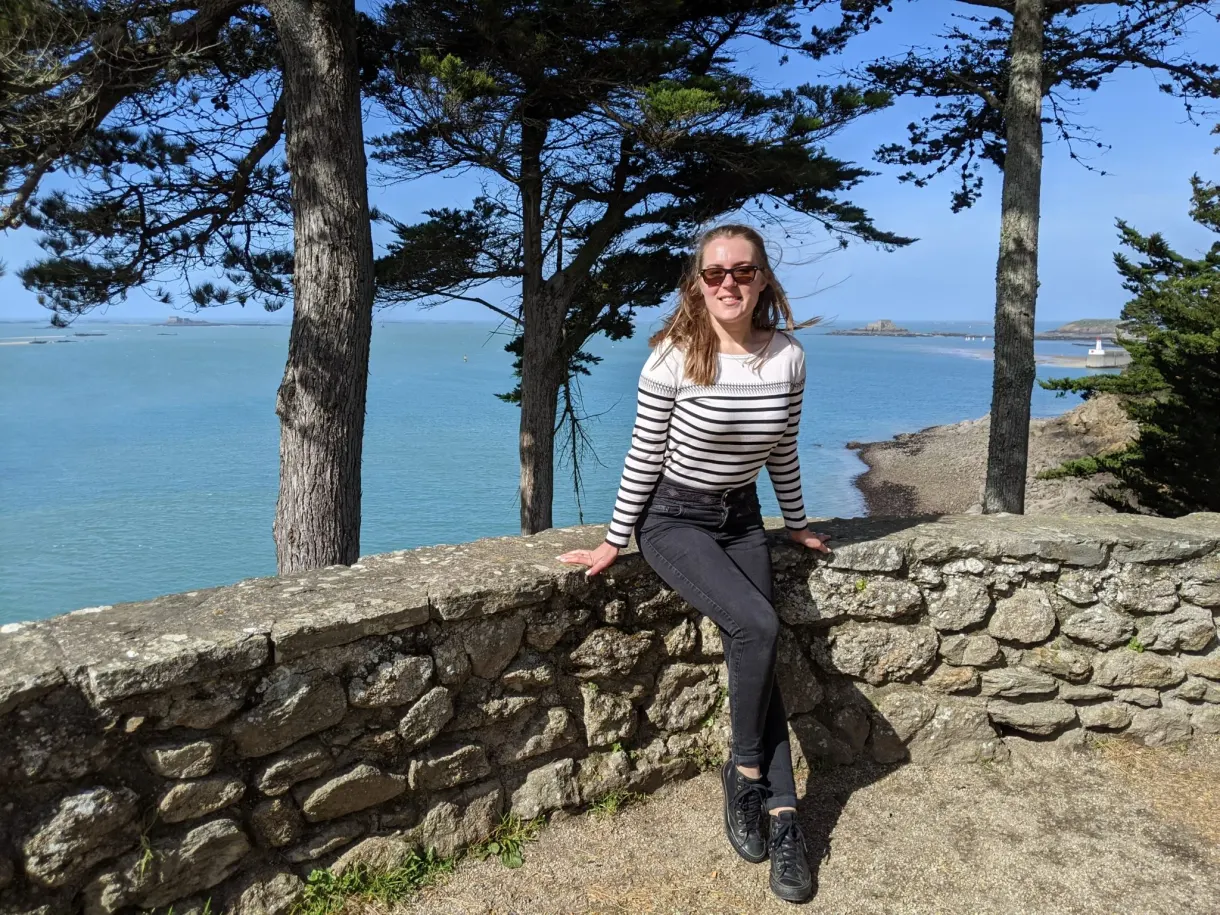 Voyageuse assise sur un muret de pierre sous les pins maritimes