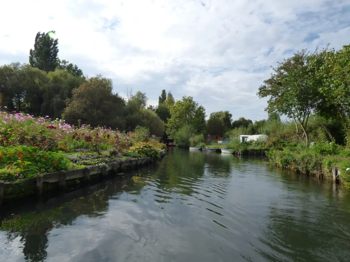 Wide canal lined with floating gardens under a cloudy sky