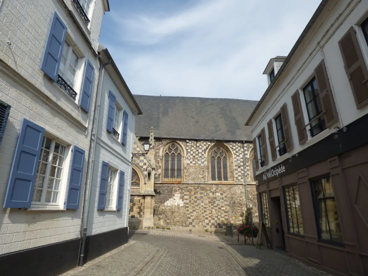 House with blue shutters next to the gothic chevet of a church