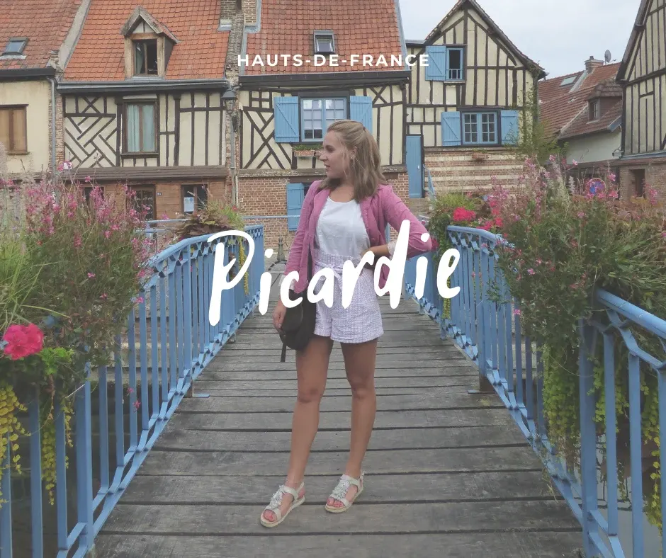 Traveller on a blue flower decked footbridge in front of half timbered houses
