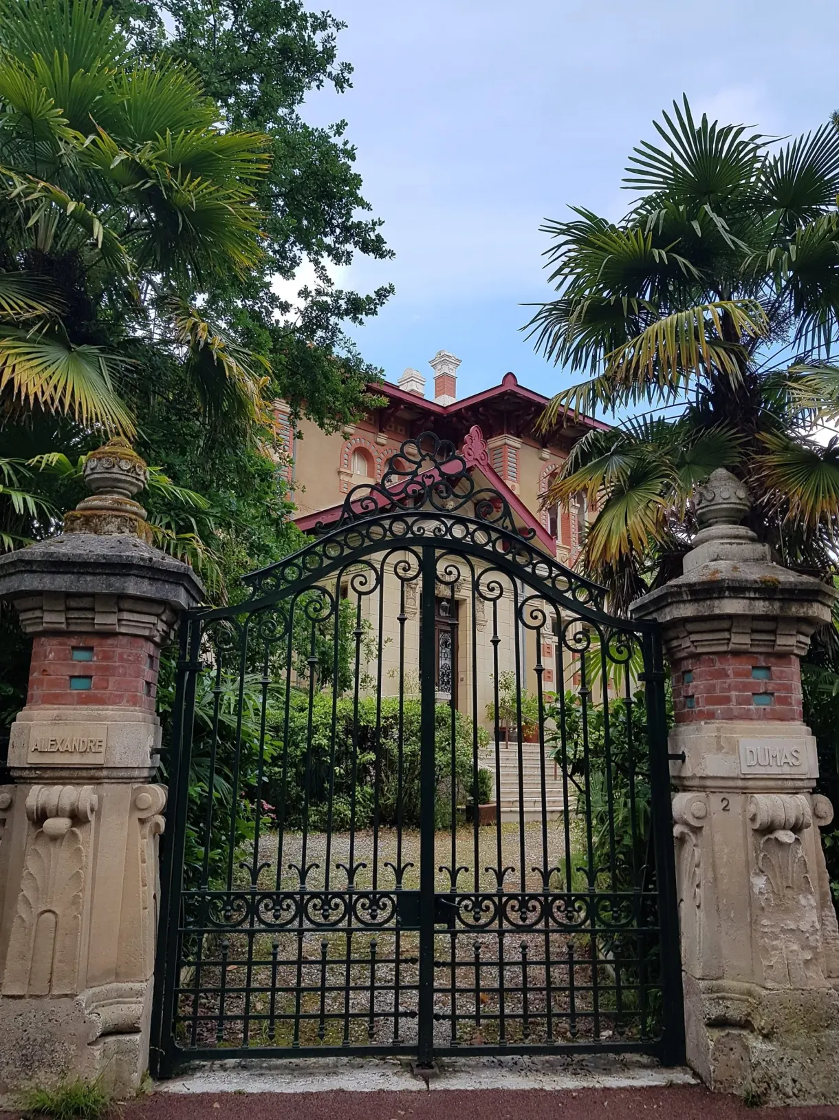 Wrought iron gate framed by palm trees in front of a villa