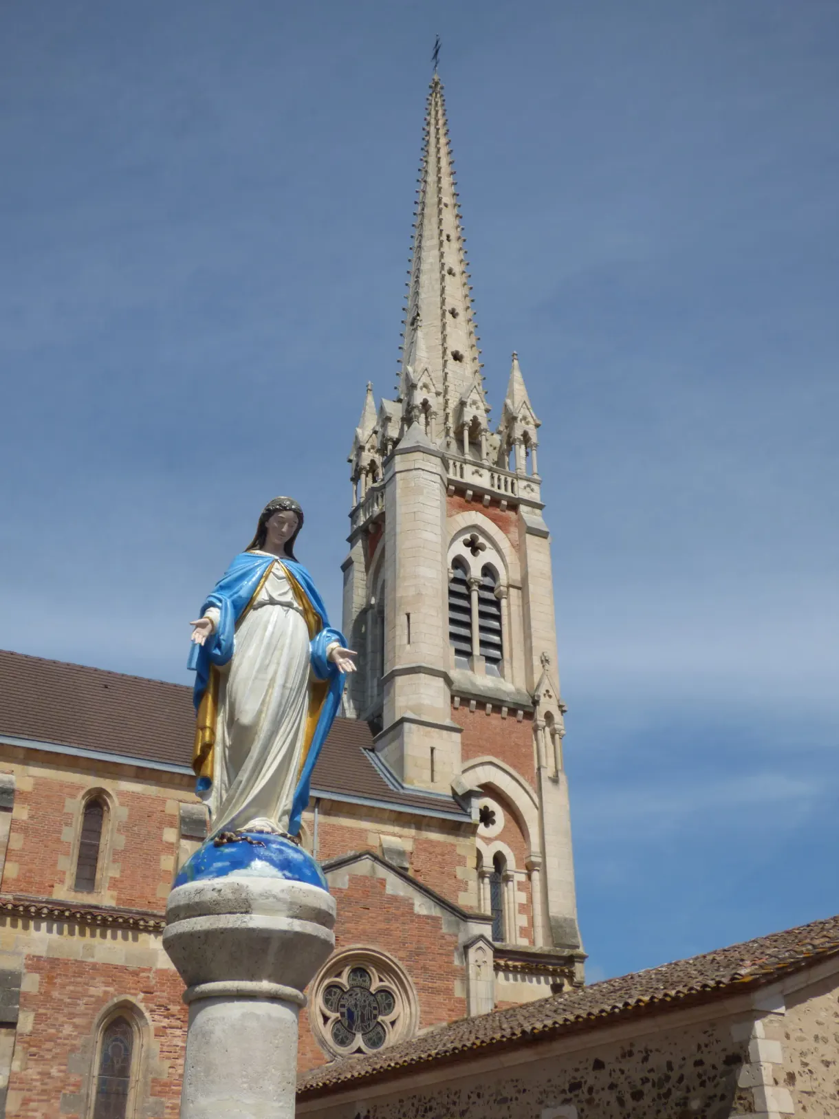 Statue of the Virgin in front of the brick bell tower of the church