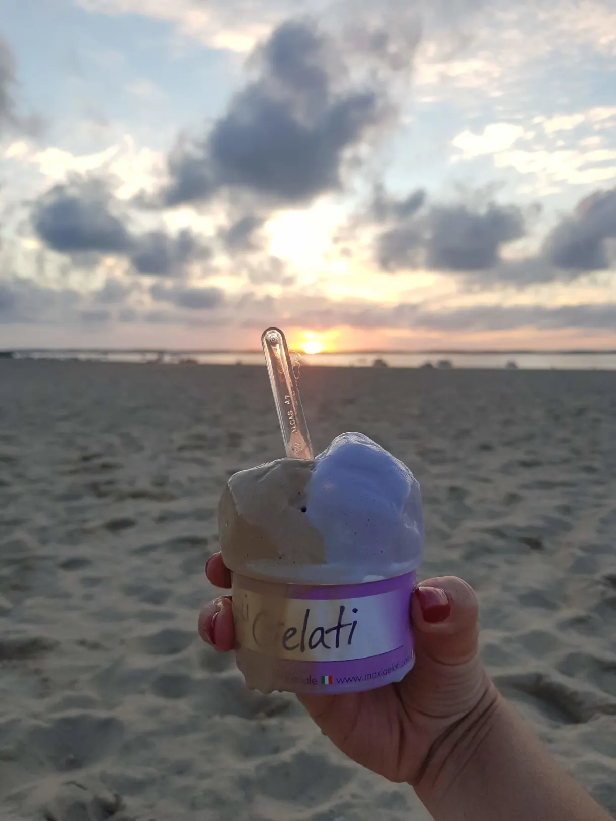 Tub of ice cream held up facing the sunset on the beach