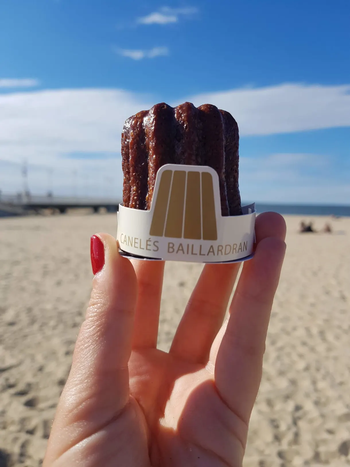 Bordeaux cannelés held in the hand in front of the beach