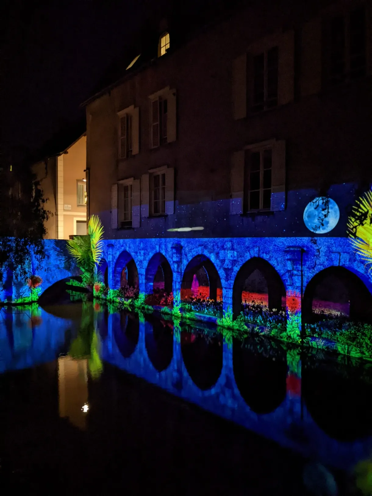 Arcades illuminées de vert et de bleu reflétées dans la rivière