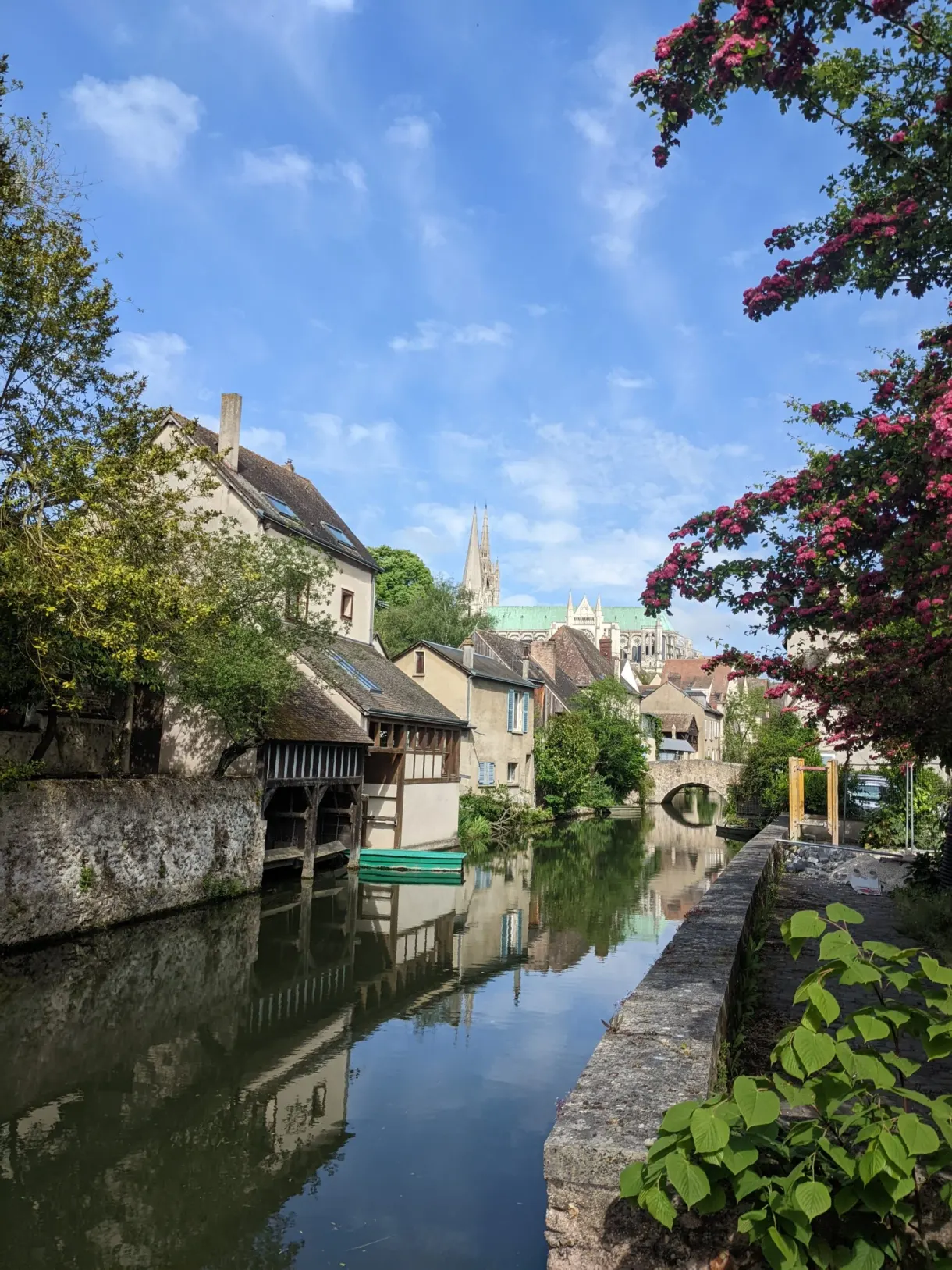 Rivière bordée de lavoirs et de rosiers grimpants, flèches au loin