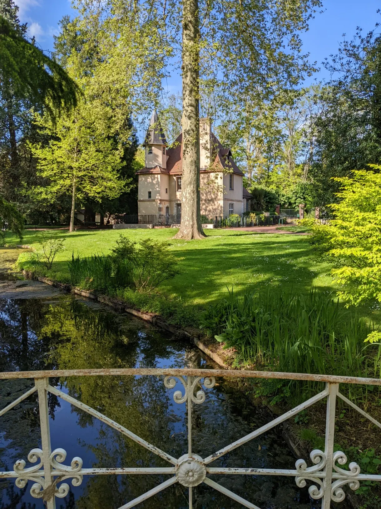 Bassin et grille de fer forgé devant la pelouse du jardin