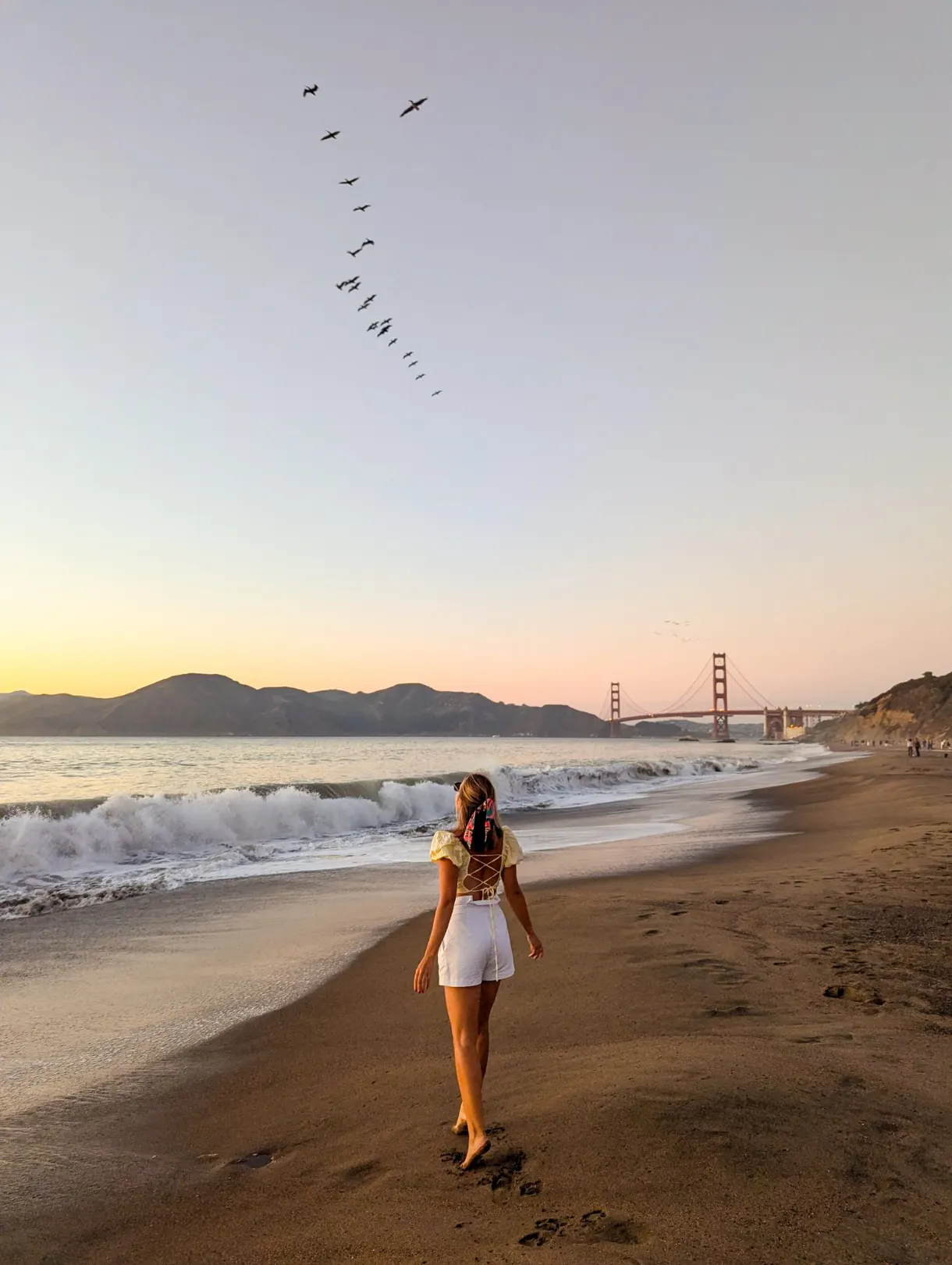 girl on a beach looking up at the sky with the Golden Gate Bridge in the background